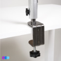 A close-up of a metal clamp securing a silver pole—part of the Pedicure Pro Package—to the edge of a white tabletop. The minimalist setup features three colored circles in the bottom left corner. Read more at Aerovex Systems (aerovexsystems.com)