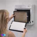 A woman with blonde hair replaces the filter of an Aerovex Systems Wall Mounted Air Purifier. The filter in her hands is clean and white, while the filter in the unit appears dirty and brown. The air purifier has a digital display with buttons above the filter slot. Read more at Aerovex Systems (aerovexsystems.com)