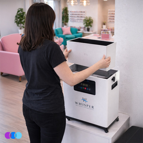 aerovex-whisper-white-filter-change-action A woman with shoulder-length brown hair, wearing a black t-shirt and jeans, places a new filter set into a white Aerovex Whisper™ salon source capture system with a digital display. The setting is a modern, brightly lit room with pink chairs and decorative shelves. Read more at Aerovex Systems (aerovexsystems.com)