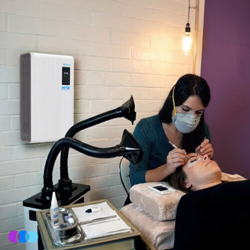 aerovex-n95-whisper-white-dual--max-white-woman-lash-studio A woman wearing an Airwave N95 mask applies eyelash extensions to a client lying on a spa bed. A dual-arm Aerovex Whisper™ source capture system and an Aerovex Max wall-mounted air purifier are in use to suction away cyanoacrylate vapors and provide fresh air. The room has white brick walls, a hanging bulb, and beauty tools on a nearby table. Read more at Aerovex Systems (aerovexsystems.com)